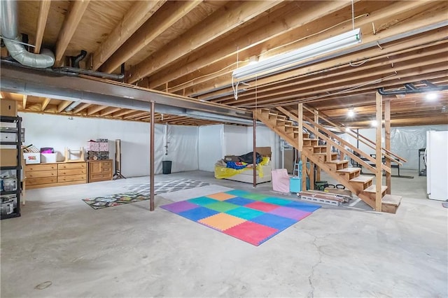 unfinished below grade area featuring stairs and freestanding refrigerator