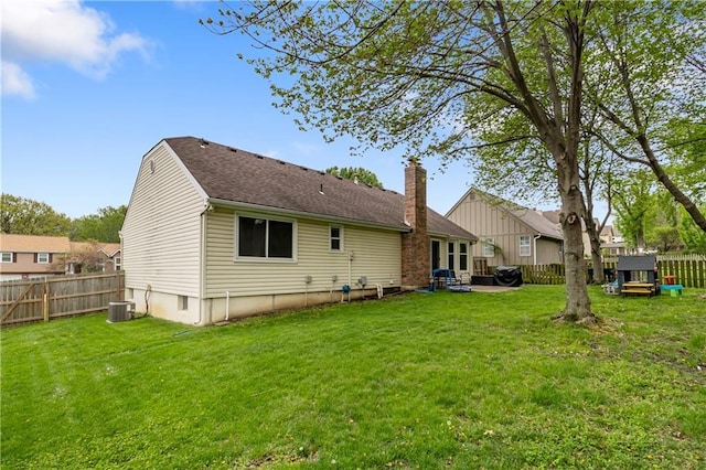 rear view of property featuring a lawn, a fenced backyard, a chimney, and cooling unit