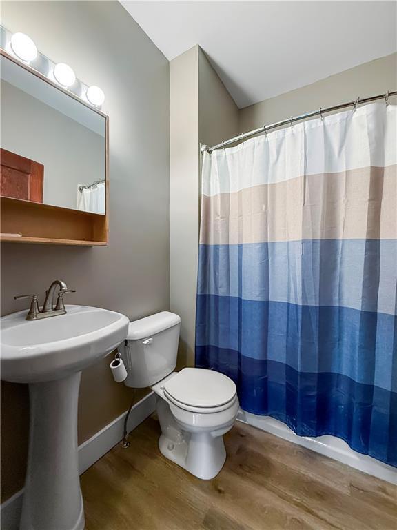 601 W 22nd St, Higginsville, MO 64037 - full bathroom featuring wood finished floors, toilet, a sink, and curtained shower
