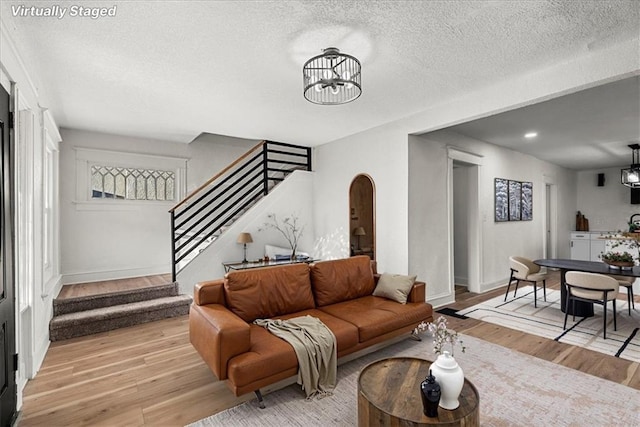living room featuring light wood-type flooring, arched walkways, an inviting chandelier, and stairs