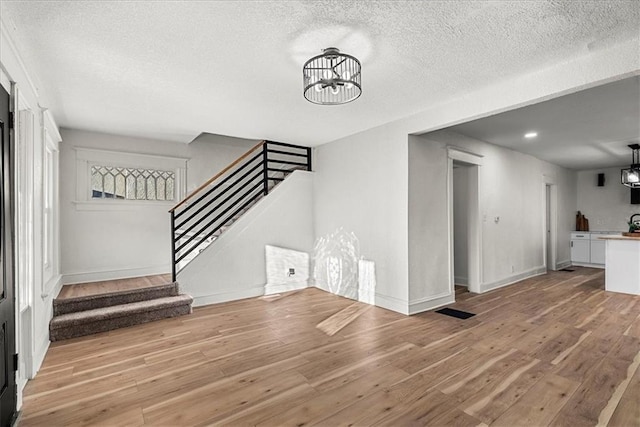 unfurnished living room with a textured ceiling, stairs, and a chandelier