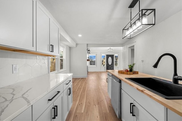 kitchen with white cabinetry, decorative backsplash, stainless steel dishwasher, light wood-style flooring, and a sink