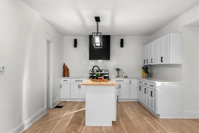 kitchen featuring stainless steel range with electric stovetop, butcher block countertops, light wood-style flooring, a kitchen island, and white cabinetry