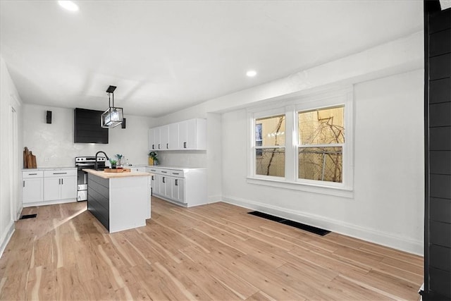 kitchen with stainless steel range with electric cooktop, a center island, baseboards, light countertops, and white cabinets