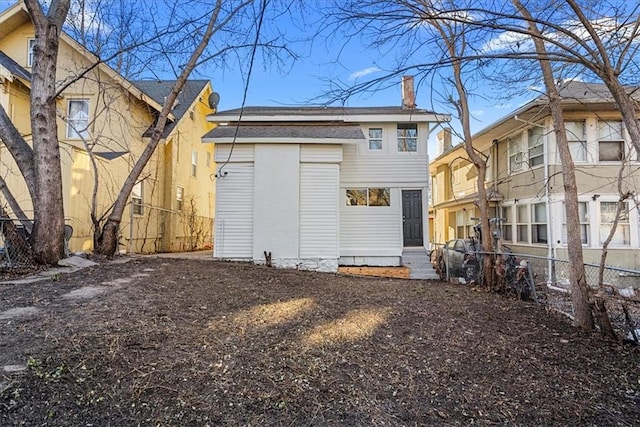 rear view of house featuring a chimney, a shingled roof, and fence