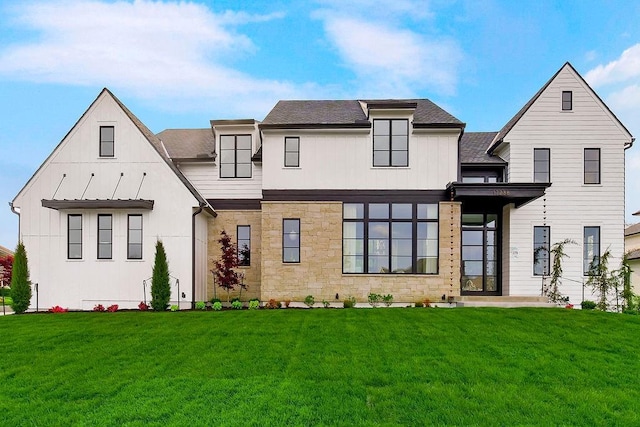 view of front of property featuring stone siding, a shingled roof, and a front yard