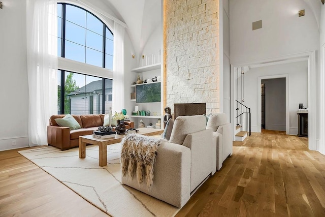 living room featuring built in features, high vaulted ceiling, a fireplace, and wood finished floors