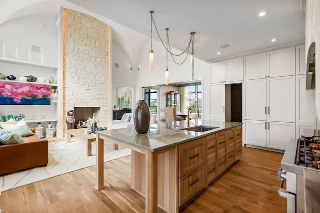 kitchen with stainless steel gas range oven, a sink, light wood finished floors, a kitchen island with sink, and open floor plan