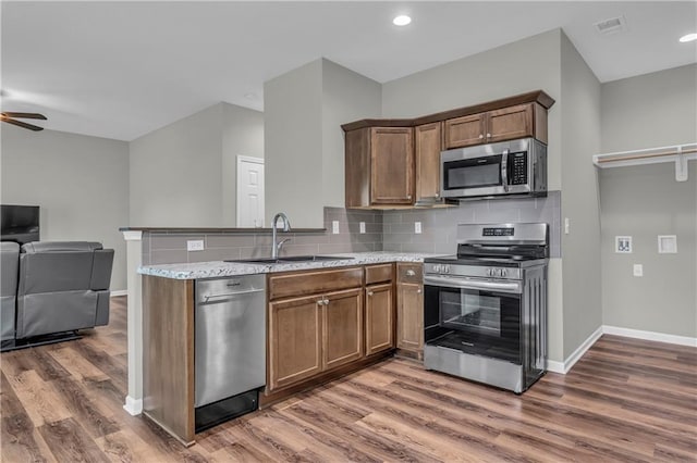 kitchen with a sink, appliances with stainless steel finishes, baseboards, open floor plan, and wood finished floors