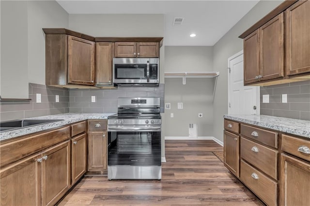 kitchen with baseboards, tasteful backsplash, light stone countertops, appliances with stainless steel finishes, and dark wood-style floors