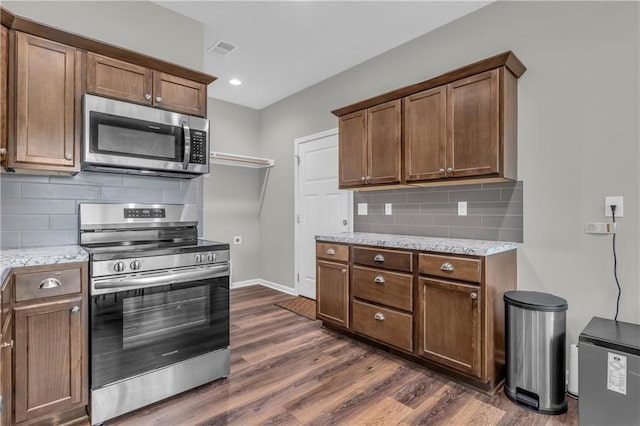 kitchen with dark wood-style floors, light stone countertops, stainless steel appliances, decorative backsplash, and visible vents