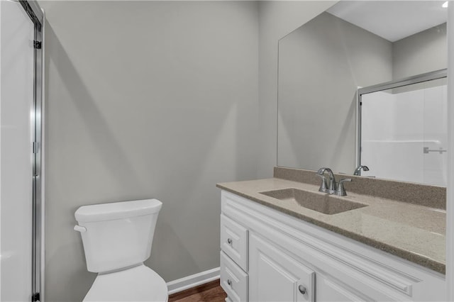 bathroom with toilet, baseboards, vanity, and a shower with door