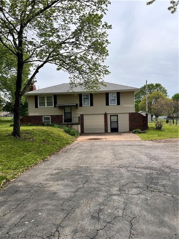 raised ranch featuring a chimney, an attached garage, a front lawn, and aphalt driveway