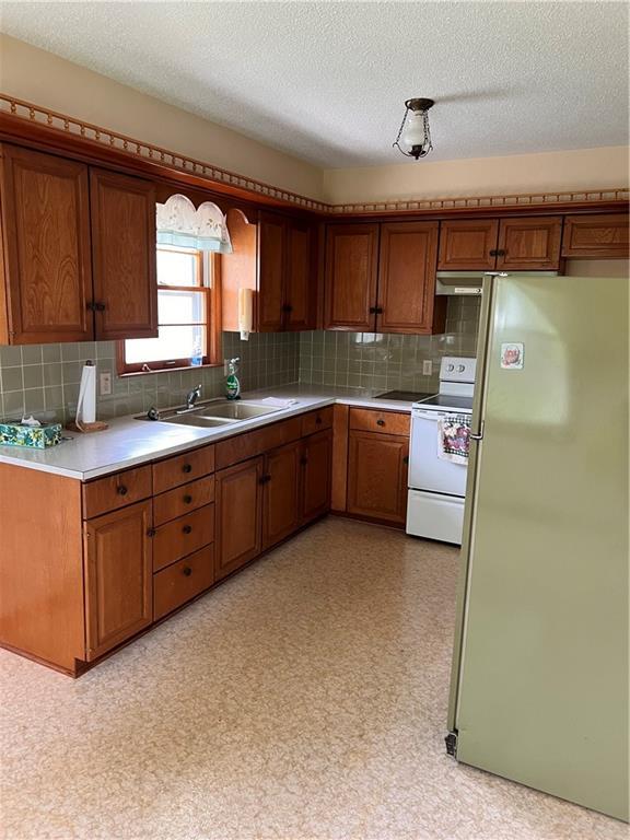 kitchen with brown cabinets, a sink, light countertops, electric stove, and freestanding refrigerator