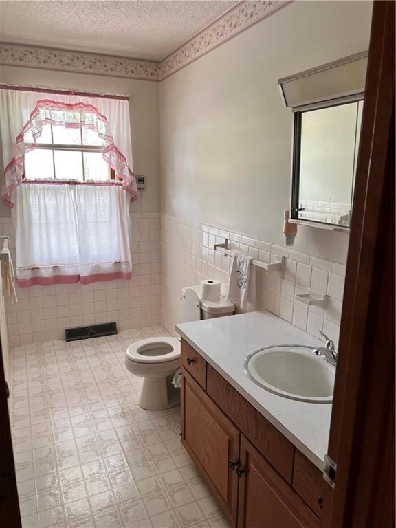 bathroom featuring vanity, toilet, tile walls, a textured ceiling, and a wainscoted wall