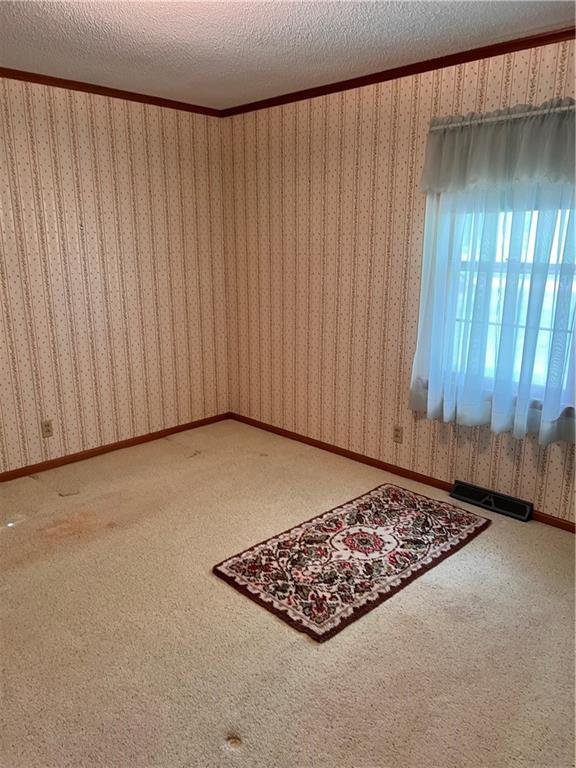 carpeted spare room with wallpapered walls and a textured ceiling