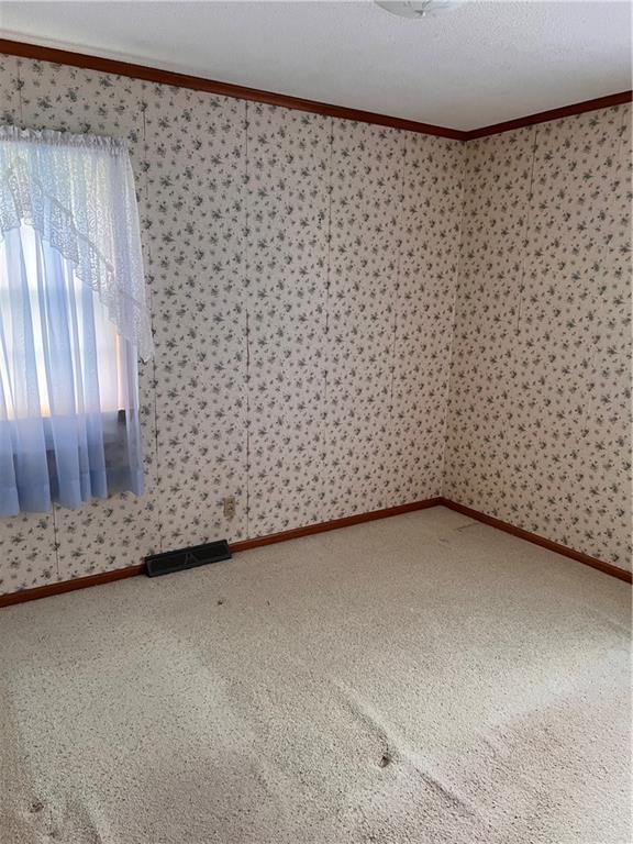 carpeted empty room featuring crown molding and wallpapered walls