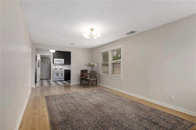 4437 N Jackson Ave, Kansas City, MO 64117 - living room featuring an inviting chandelier, light wood finished floors, a textured ceiling, baseboards, and visible vents