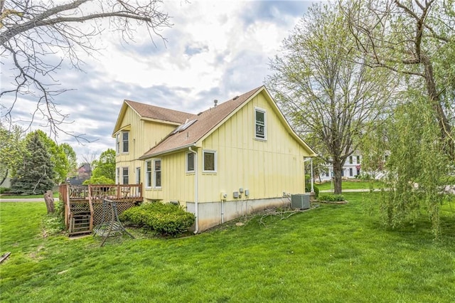 view of side of property featuring a deck, a yard, board and batten siding, roof with shingles, and central AC unit