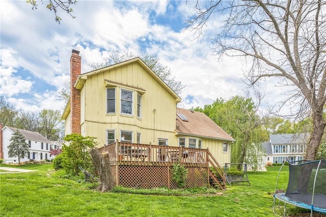 rear view of property with a trampoline, a chimney, a deck, a lawn, and board and batten siding