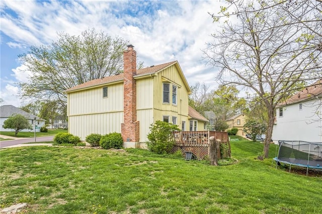 view of side of home featuring a trampoline, a deck, a chimney, a yard, and board and batten siding