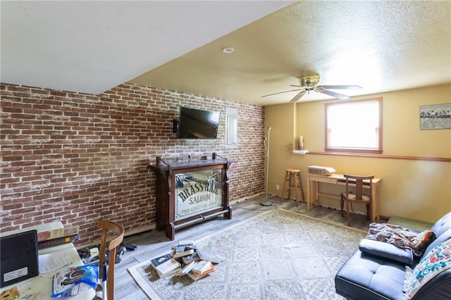 living room with wood finished floors, a ceiling fan, and brick wall