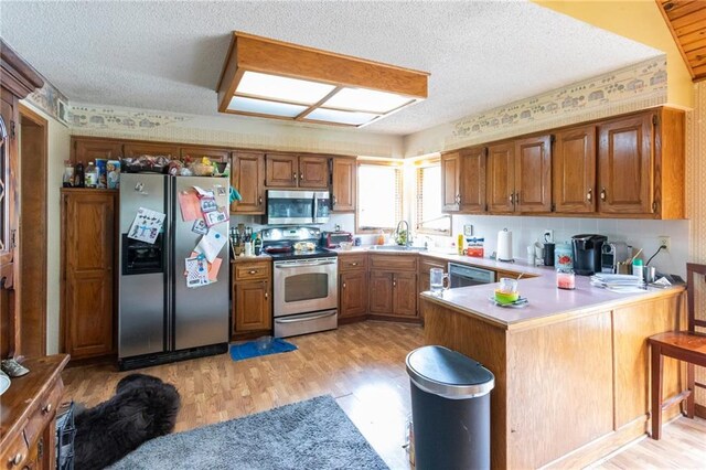 kitchen with stainless steel appliances, a peninsula, light wood-type flooring, brown cabinetry, and a sink