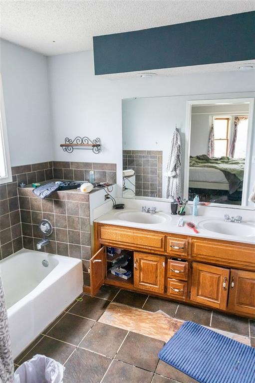 full bath featuring healthy amount of natural light, a textured ceiling, a garden tub, double vanity, and tile patterned floors