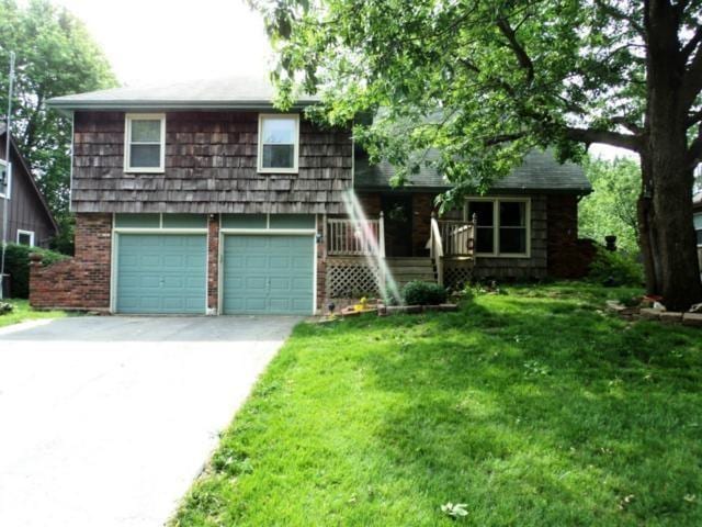 split level home with concrete driveway, brick siding, an attached garage, and a front lawn