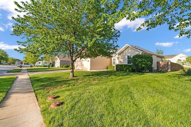 view of yard with fence, an attached garage, and driveway