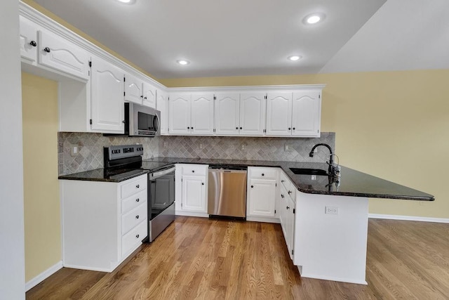 kitchen with a peninsula, light wood-type flooring, white cabinets, a sink, and stainless steel appliances