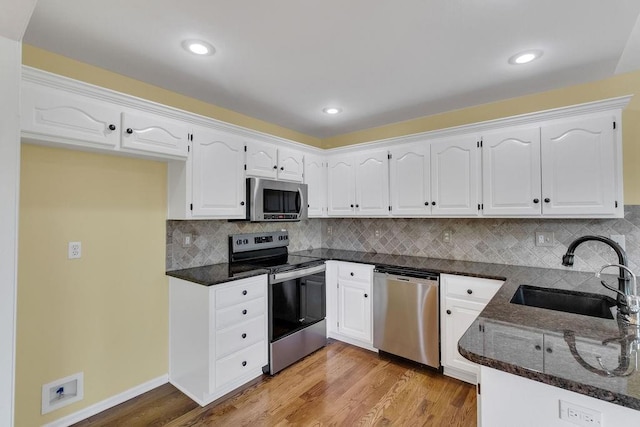 kitchen with dark stone counters, stainless steel appliances, white cabinetry, and a sink
