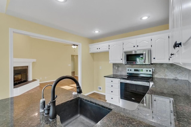 kitchen with appliances with stainless steel finishes, tasteful backsplash, a sink, white cabinets, and dark stone counters