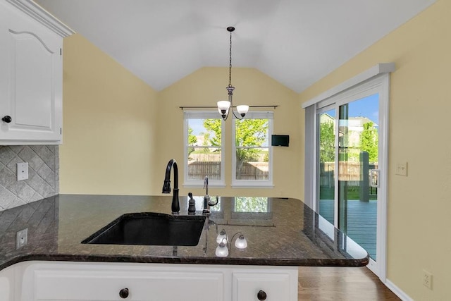 kitchen with a sink, dark stone countertops, backsplash, and a chandelier