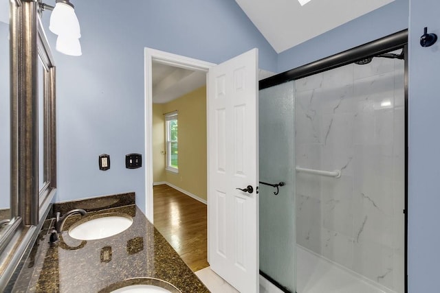 bathroom with a sink, double vanity, wood finished floors, vaulted ceiling, and a stall shower