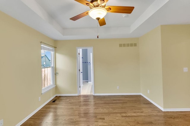 unfurnished room featuring visible vents, wood finished floors, baseboards, ceiling fan, and a tray ceiling