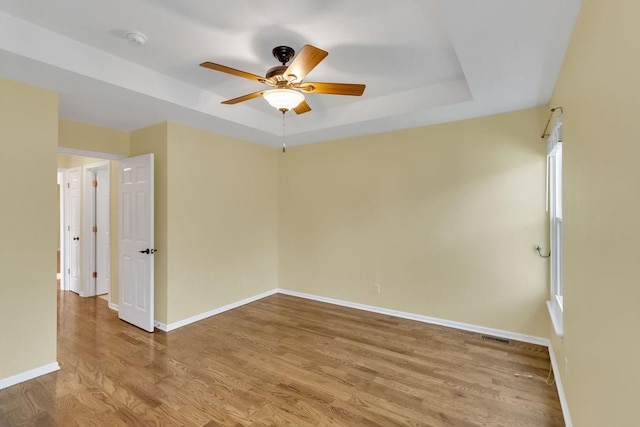 empty room featuring baseboards, ceiling fan, wood finished floors, and a raised ceiling