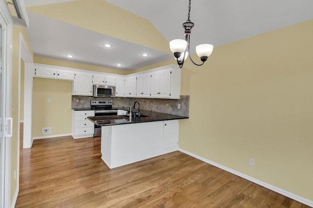 kitchen with an inviting chandelier, a peninsula, dark countertops, white cabinetry, and stainless steel appliances