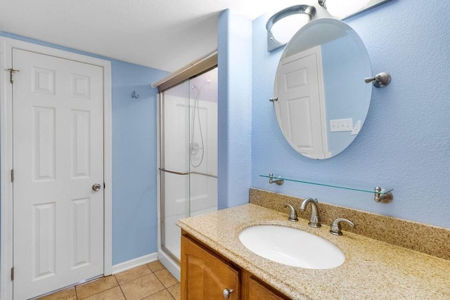 full bath featuring vanity, tile patterned flooring, baseboards, and a stall shower