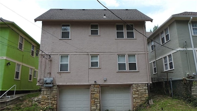back of property with fence, stucco siding, an attached garage, and stone siding