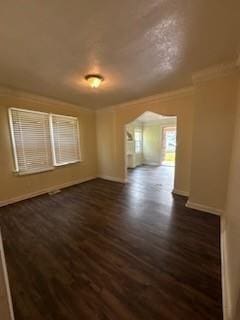 empty room featuring dark wood-style flooring, ornamental molding, and baseboards