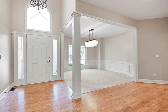 foyer entrance with a chandelier, light wood finished floors, and decorative columns