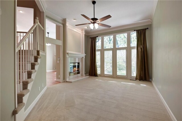 unfurnished living room featuring ornamental molding, ceiling fan, carpet flooring, stairway, and baseboards