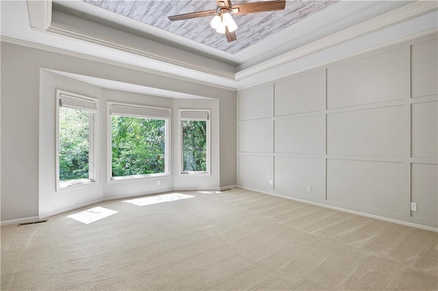 unfurnished room featuring a raised ceiling, healthy amount of natural light, light carpet, ceiling fan, and ornamental molding
