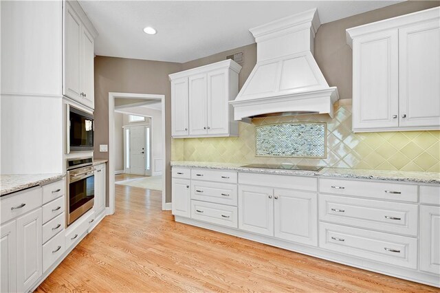 kitchen with black appliances, premium range hood, backsplash, white cabinetry, and recessed lighting