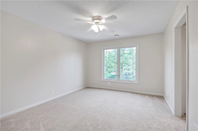 empty room featuring light colored carpet, ceiling fan, a textured ceiling, and baseboards