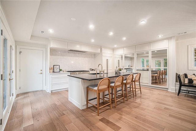 9440 Manor Rd, Leawood, KS 66206 - kitchen with light wood-type flooring, white cabinets, decorative backsplash, a sink, and a kitchen breakfast bar