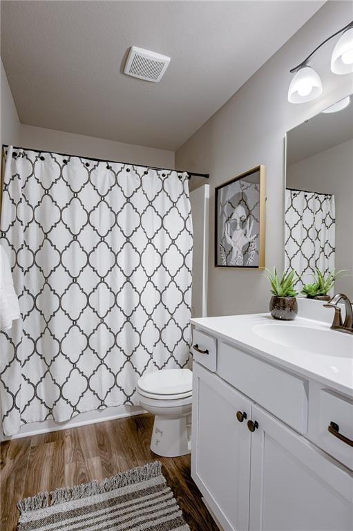 full bath featuring vanity, toilet, visible vents, wood finished floors, and a shower with shower curtain
