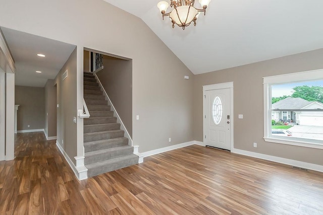 foyer entrance with visible vents, wood finished floors, vaulted ceiling, and stairway