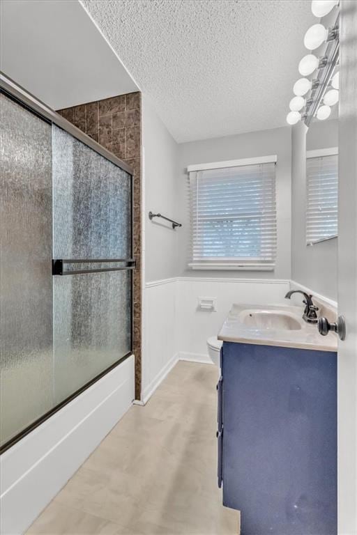 7934 Maple St, Prairie Village, KS 66208 - bathroom featuring a textured ceiling, combined bath / shower with glass door, vanity, a wainscoted wall, and toilet